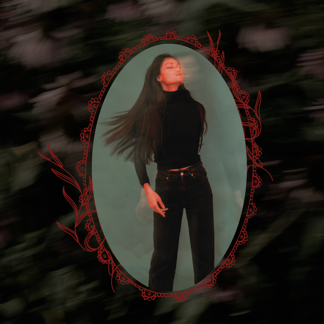 A woman with long dark hair stands in front of an oval mirror, wearing a black turtleneck and black jeans. The mirror is framed by a red ornate border, set against a dark, blurred background.